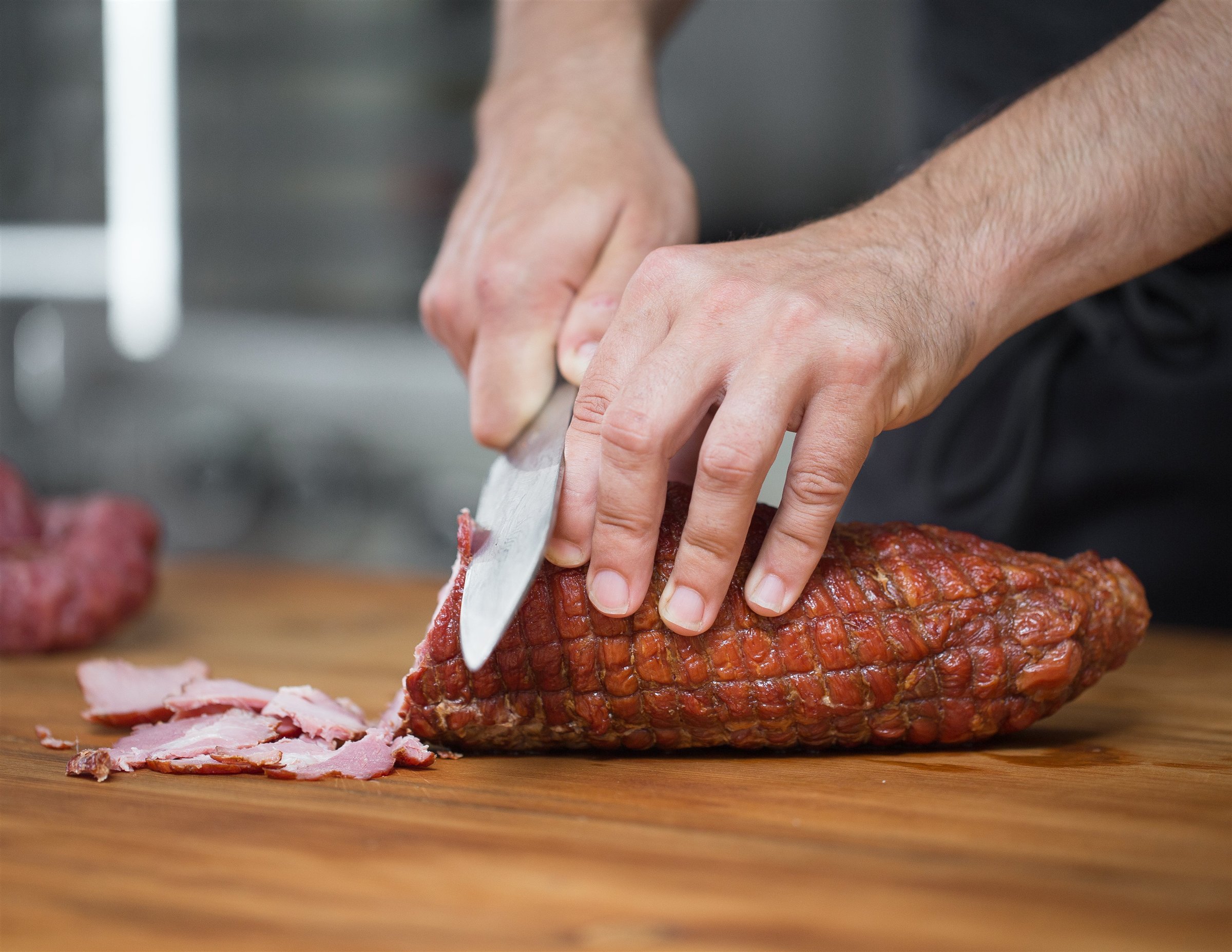 Hands slicing a cured product on a wooden work surface