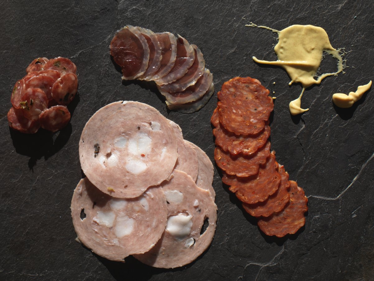 Assorted sliced charcuterie arranged on dark slate