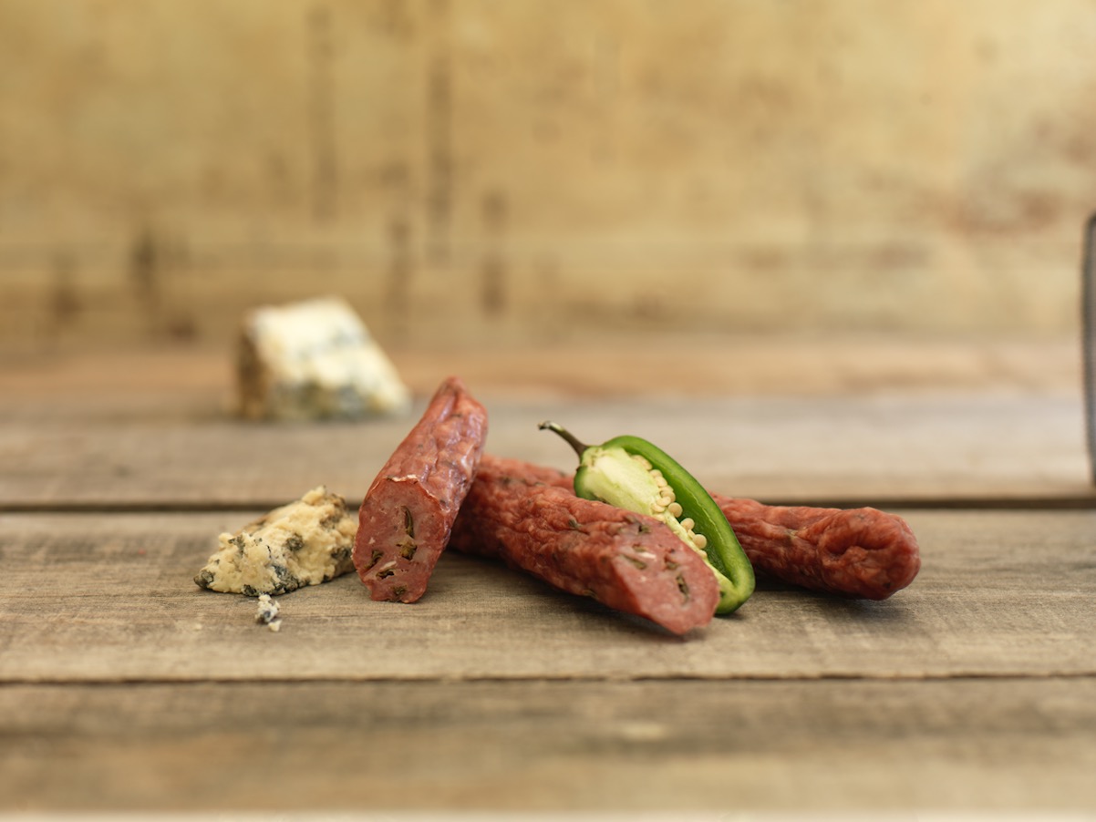 Jalapeno and blue cheese salami with sliced pieces on a wooden surface